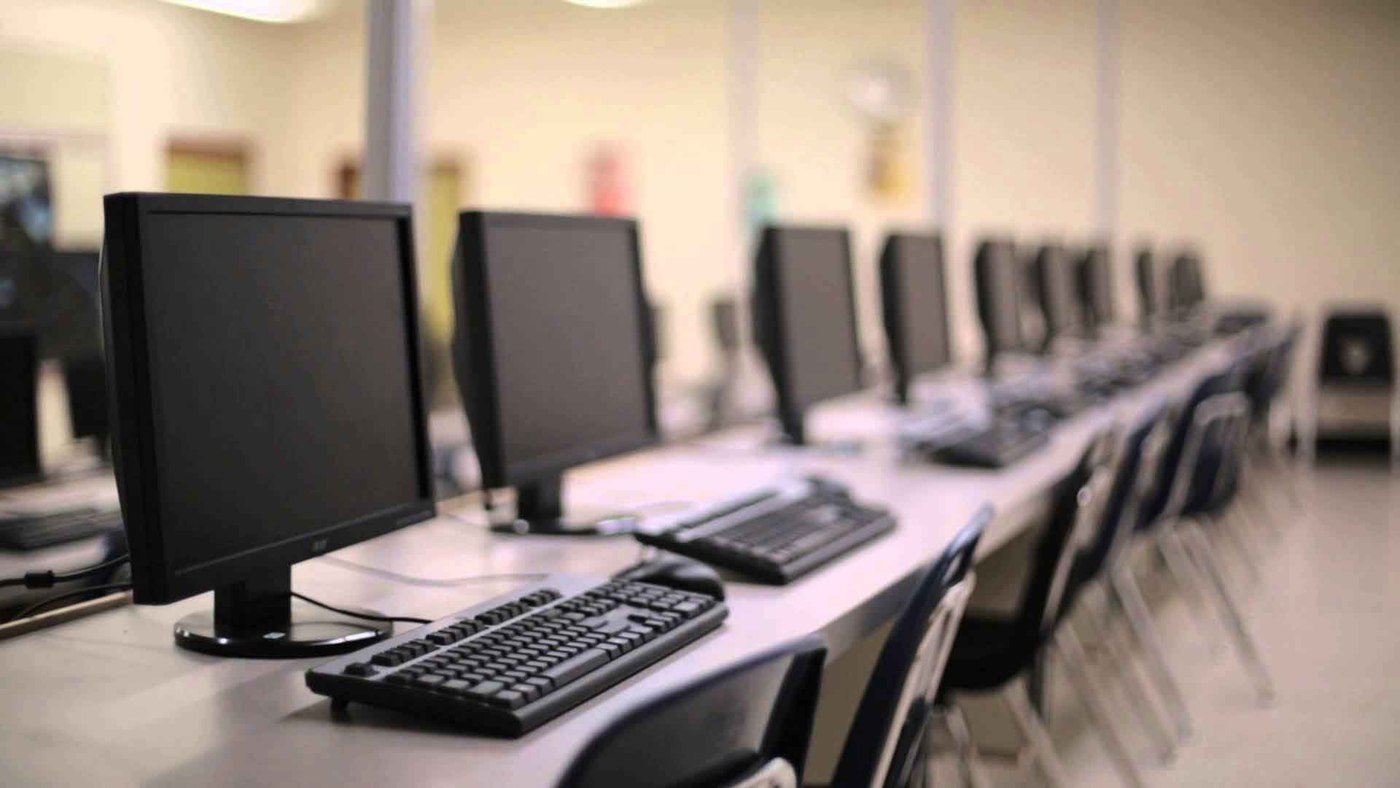 Laboratório de informática com computadores em fileira, pronto para aula